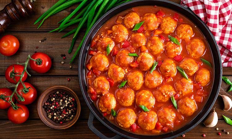 albondigas en salsa, spanish meatballs in tomato sauce in a pan with fresh ingredients on the side