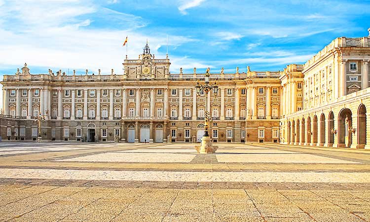 palacio real, exterior building of the royal palace in madrid with courtyard in the foreground and spanish flag on the roof