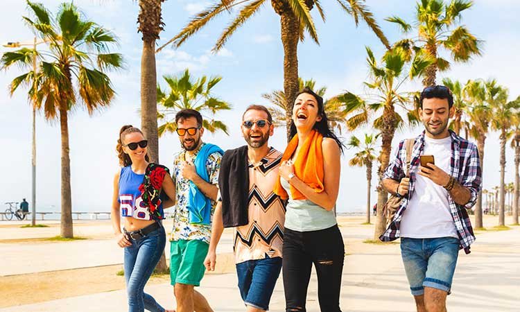 auswanderer in Barcelona, lachende Freunde in Barceloneta auf dem Weg zwischen Palmen in Sommerkleidung